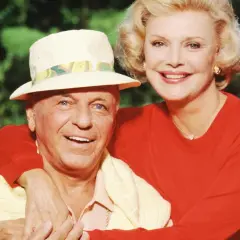 Frank Sinatra z żoną Barbarą, uśmiechnięci, w słoneczny dzień na tle zieleni.