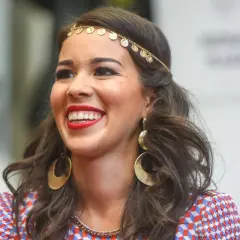 Uśmiechnięta Tamara Gonzalez Perea w złotej biżuterii i kolorowej sukience.