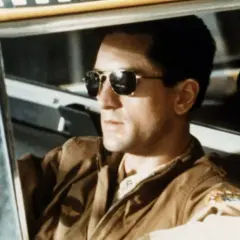 Robert De Niro w okularach przeciwsłonecznych za kierownicą taksówki. Ikona kina, jak w wielu filmach z jego udziałem.