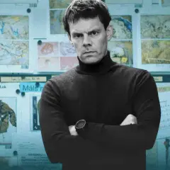 Detektyw Harry Hole w czarnym golfie, z rękami skrzyżowanymi na piersi, stoi przed tablicą pełną dowodów. To kolejny przypadek w jego karierze, jak w każdym serialu z jego udziałem.