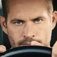 Paul Walker, gwiazda filmów o szybkich samochodach, z intensywnym spojrzeniem za kierownicą.
