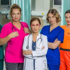 Pięć kobiet w strojach medycznych, obsada serialu "Szpital św. Anny", pozuje do zdjęcia w szpitalnej sali.
