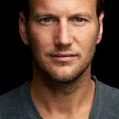 Patrick Wilson, znany z wielu filmów, z niebieskimi oczami i lekkim zarostem, patrzy wprost na widza.
