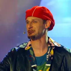 Michał Wójcik z kabaretu, w czerwonej beretce i kolorowej koszuli, na scenie.