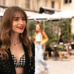 Emily w Paryżu, uśmiechnięta, w stylowej stylizacji, na tle paryskiej kawiarni.