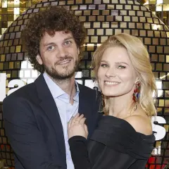 Anna Głogowska z partnerem pozują na tle błyszczącej, złotej ściany.