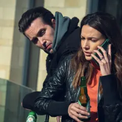 Kobieta rozmawia przez telefon, trzymając piwo. Mężczyzna za nią patrzy z podejrzliwością. Już mnie nie oszukasz.