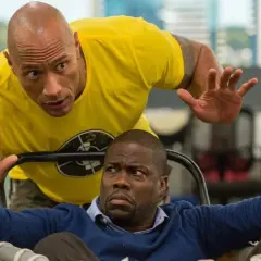 Dwayne Johnson w żółtej koszulce i Kevin Hart w niebieskim swetrze, w scenie akcji z jednego z ich filmów.