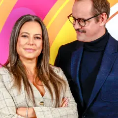 Para z uśmiechem na tle tęczowych pasów. Kobieta w beżowej marynarce, mężczyzna w okularach i granatowej marynarce. Czy to Jakub Wons z żoną?