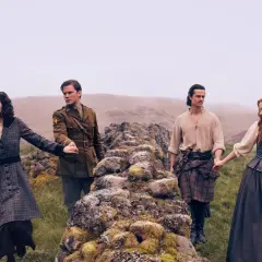 Cztery postacie na tle mglistych wzgórz. Dwie pary trzymają się za ręce, sugerując więzi z serialu **Outlander: Krew z krwi**.