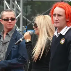 Ich troje wokalistki na scenie, z mikrofonami w dłoniach. Jeden z nich ma ogniste, pomarańczowe włosy.
