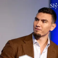 Młody mężczyzna w brązowej marynarce, z zarostem. Conan Kaźmierski wiek to temat dyskusji, ale jego pewność siebie mówi wiele.