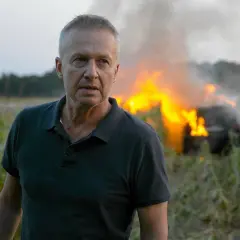 Mężczyzna w polu kukurydzy, za nim płonący samochód. Pitbull nowe porządki.