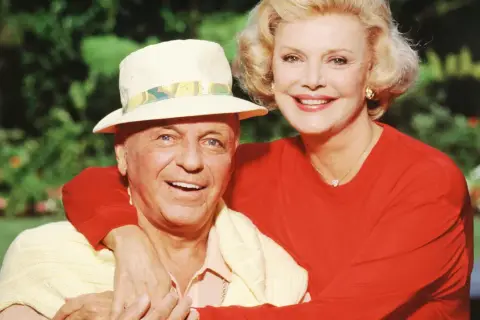 Frank Sinatra z żoną Barbarą, uśmiechnięci, w słoneczny dzień na tle zieleni.