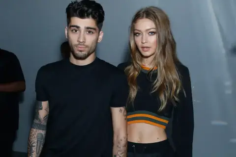 Zayn Malik i Gigi Hadid pozują razem, oboje ubrani na czarno. Zayn ma tatuaże na ramionach, a Gigi odsłania brzuch w krótkim topie.