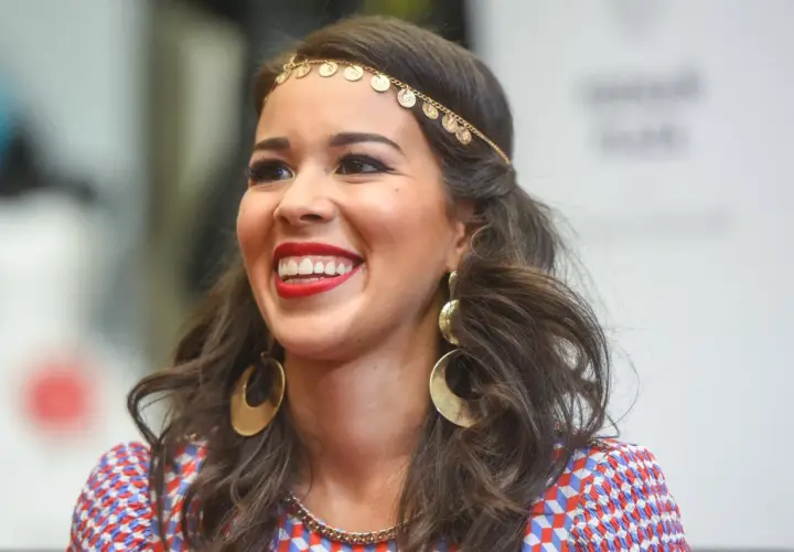 Uśmiechnięta Tamara Gonzalez Perea w złotej biżuterii i kolorowej sukience.