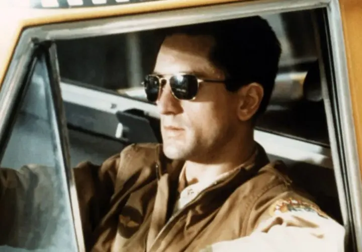 Robert De Niro w okularach przeciwsłonecznych za kierownicą taksówki. Ikona kina, jak w wielu filmach z jego udziałem.
