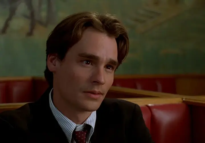 Robert Sean Leonard w garniturze, w tle zielona ściana z malowidłem. Jego filmy i seriale to klasyka.
