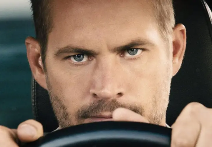 Paul Walker, gwiazda filmów o szybkich samochodach, z intensywnym spojrzeniem za kierownicą.