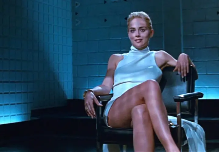 Sharon Stone w białej sukience, siedząca w fotelu, ikona kina. Jej role w filmach zapisały się w historii.