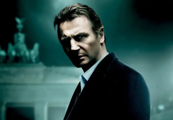 Liam Neeson w mrocznym garniturze, zdeterminowany. Tło sugeruje scenę z jednego z jego filmów akcji.