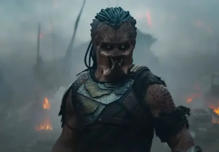 Predator w strefie zagrożenia, otoczony dymem i płomieniami. Jego groźna twarz i zbroja budzą strach.