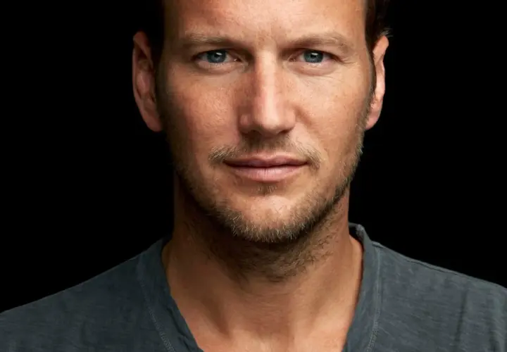 Patrick Wilson, znany z wielu filmów, z niebieskimi oczami i lekkim zarostem, patrzy wprost na widza.