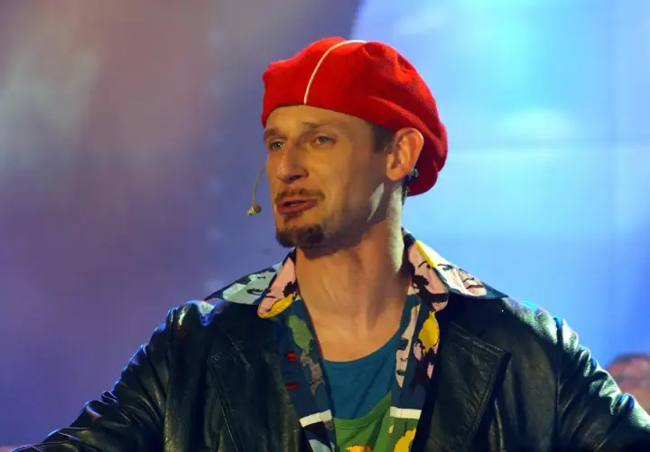 Michał Wójcik z kabaretu, w czerwonej beretce i kolorowej koszuli, na scenie.