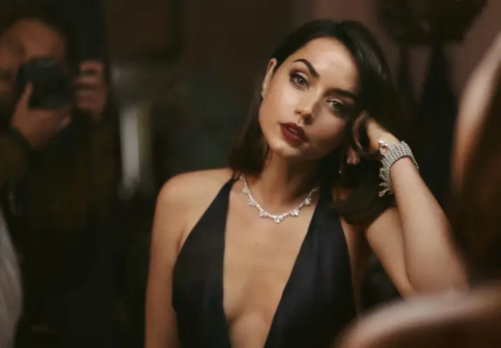 Elegancka Ana de Armas w czarnej sukni i biżuterii, jak z najlepszych filmów. W tle widać fotografa.