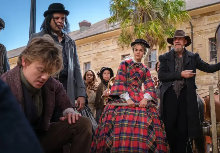 Młody chłopak, jak **the artful dodger**, pochyla się, podczas gdy tłum ludzi w strojach z epoki obserwuje coś poza kadrem.
