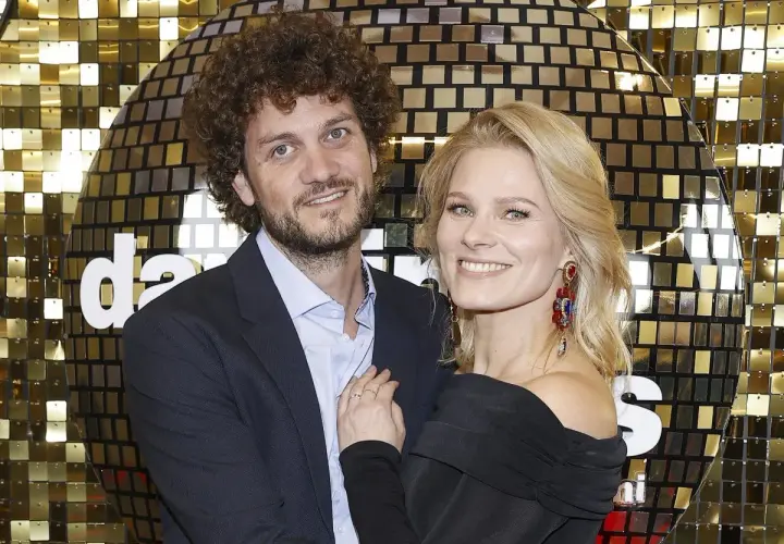 Anna Głogowska z partnerem pozują na tle błyszczącej, złotej ściany.