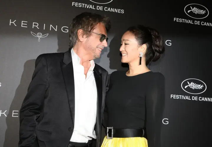 Jean-Michel Jarre i jego żona, Gong Li, uśmiechają się do siebie na tle napisu "Festival de Cannes".