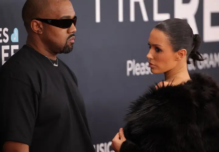 Kanye West i Bianca na ściance. Kanye w czarnym t-shircie i okularach, Bianca w futrzanym płaszczu.