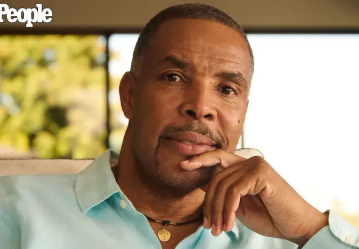 Eriq La Salle, zamyślony, opiera podbródek na dłoni. Ma na sobie błękitną koszulę i naszyjnik.