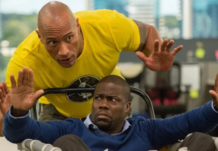 Dwayne Johnson w żółtej koszulce i Kevin Hart w niebieskim swetrze, w scenie akcji z jednego z ich filmów.