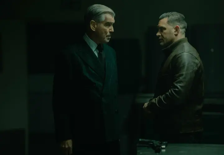 Dwóch mężczyzn w mrocznym pomieszczeniu, jeden w eleganckim garniturze, drugi w skórzanej kurtce. Napięta atmosfera, jakby szykowali się do akcji w mobland season 2.