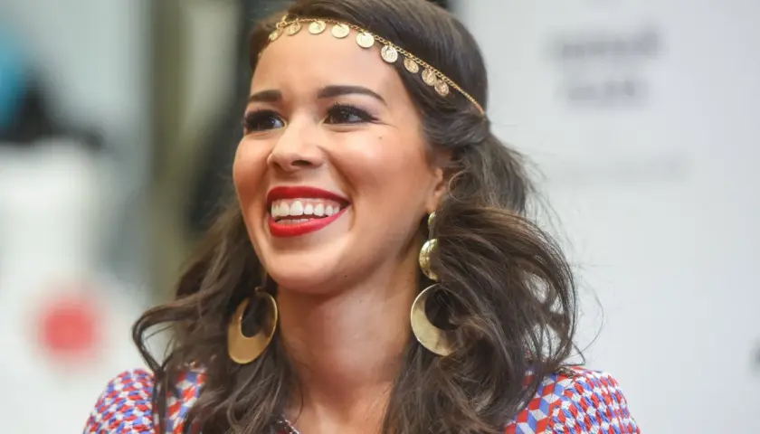 Uśmiechnięta Tamara Gonzalez Perea w złotej biżuterii i kolorowej sukience.