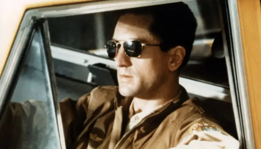 Robert De Niro w okularach przeciwsłonecznych za kierownicą taksówki. Ikona kina, jak w wielu filmach z jego udziałem.