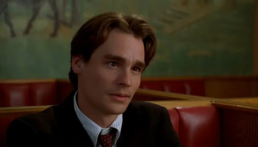 Robert Sean Leonard w garniturze, w tle zielona ściana z malowidłem. Jego filmy i seriale to klasyka.