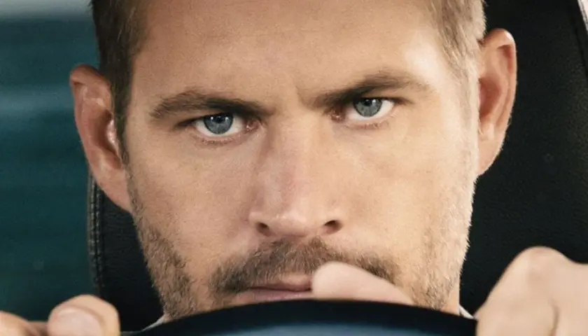 Paul Walker, gwiazda filmów o szybkich samochodach, z intensywnym spojrzeniem za kierownicą.