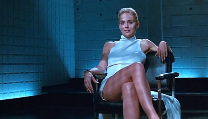 Sharon Stone w białej sukience, siedząca w fotelu, ikona kina. Jej role w filmach zapisały się w historii.