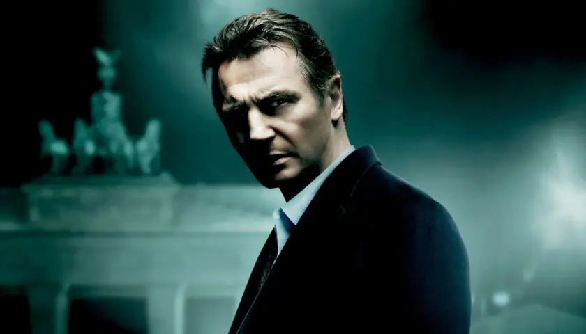Liam Neeson w mrocznym garniturze, zdeterminowany. Tło sugeruje scenę z jednego z jego filmów akcji.