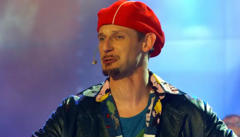 Michał Wójcik z kabaretu, w czerwonej beretce i kolorowej koszuli, na scenie.
