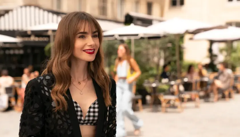 Emily w Paryżu, uśmiechnięta, w stylowej stylizacji, na tle paryskiej kawiarni.