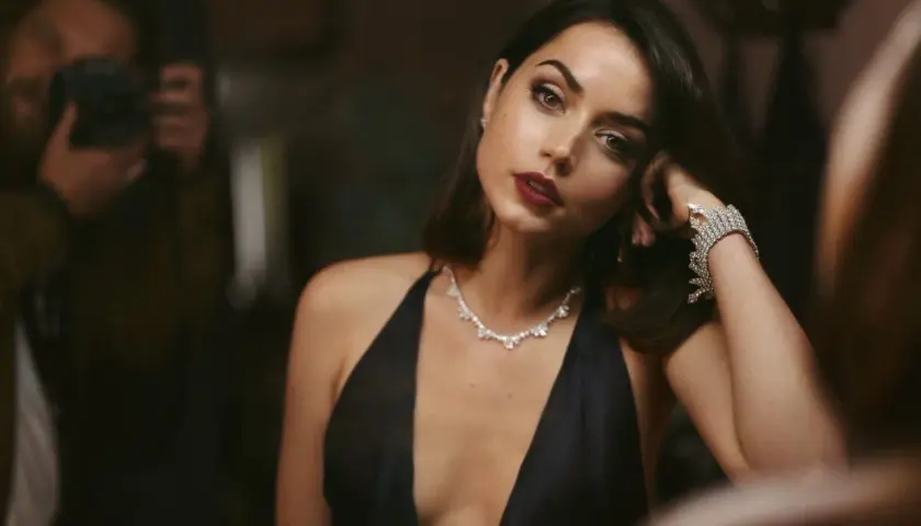 Elegancka Ana de Armas w czarnej sukni i biżuterii, jak z najlepszych filmów. W tle widać fotografa.