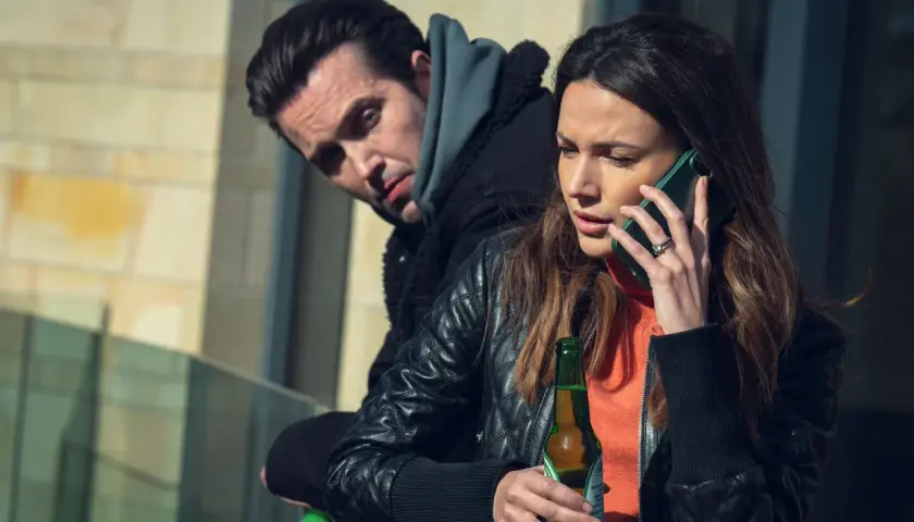 Kobieta rozmawia przez telefon, trzymając piwo. Mężczyzna za nią patrzy z podejrzliwością. Już mnie nie oszukasz.