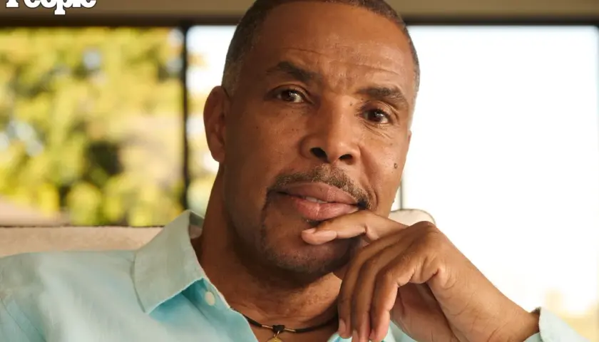 Eriq La Salle, zamyślony, opiera podbródek na dłoni. Ma na sobie błękitną koszulę i naszyjnik.