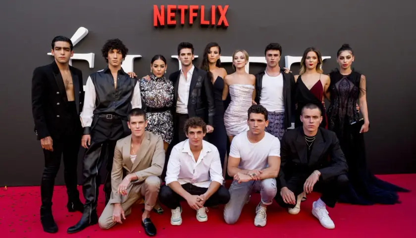 Cała obsada serialu "Szkoła dla elity" pozuje na czerwonym dywanie przed logo Netflix.