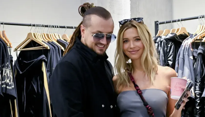 Sandra Kubicka i Baron uśmiechają się do zdjęcia, stojąc przed wieszakami z ubraniami.