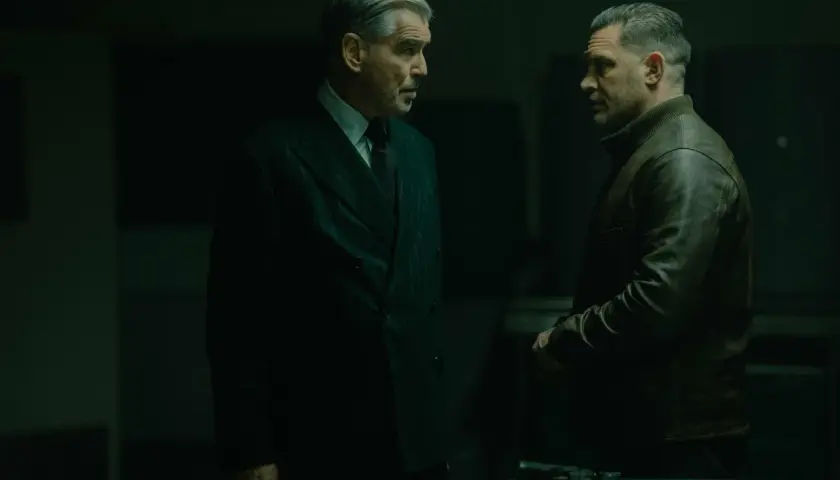 Dwóch mężczyzn w mrocznym pomieszczeniu, jeden w eleganckim garniturze, drugi w skórzanej kurtce. Napięta atmosfera, jakby szykowali się do akcji w mobland season 2.